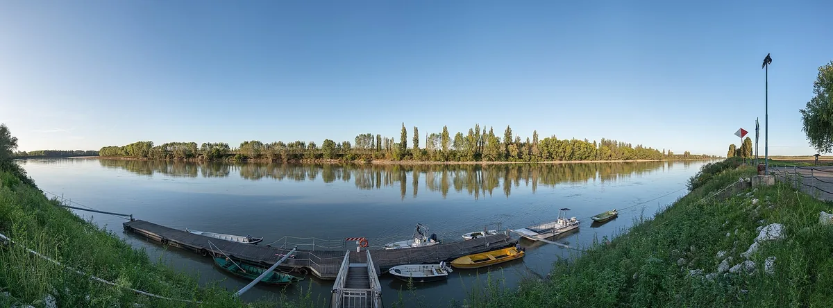 Panorama del Po fermo che riflette i pioppi, con un pontile e barche piccole