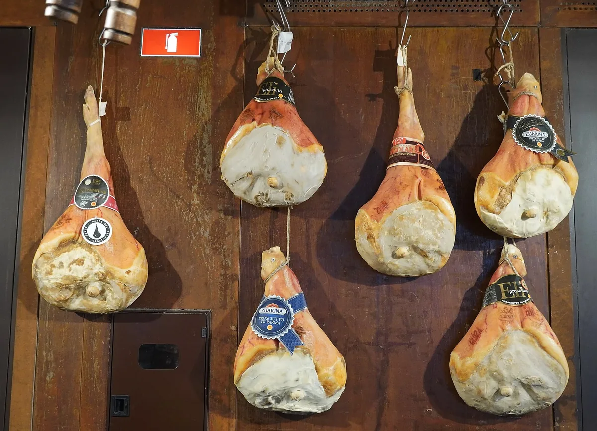 Sieben Prosciutto di Parma Schinken mit Markenaufklebern an einer Holzwand