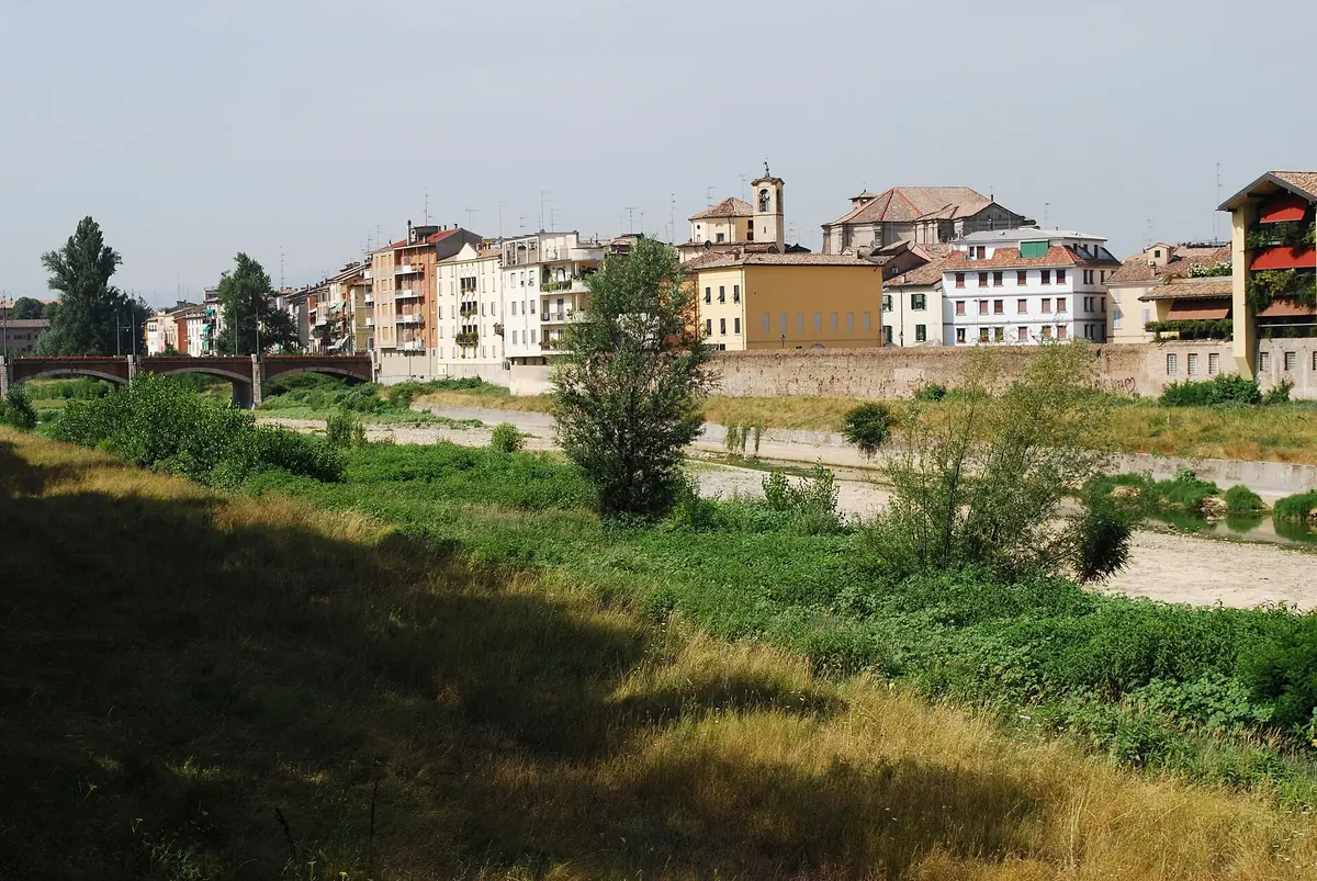 Pastellfarbene Häuser von Parmas Oltretorrente, gesehen über das grasbewachsene Bett des Parma-Flusses