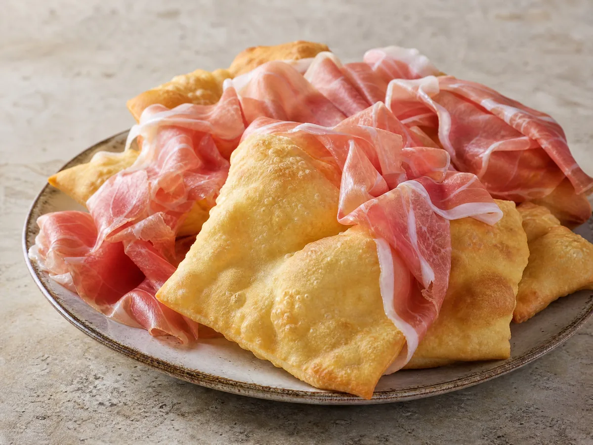 Goldbraune, aufgeblähte Quadrate aus frittiertem Teig, serviert mit drapierten Scheiben Prosciutto di Parma
