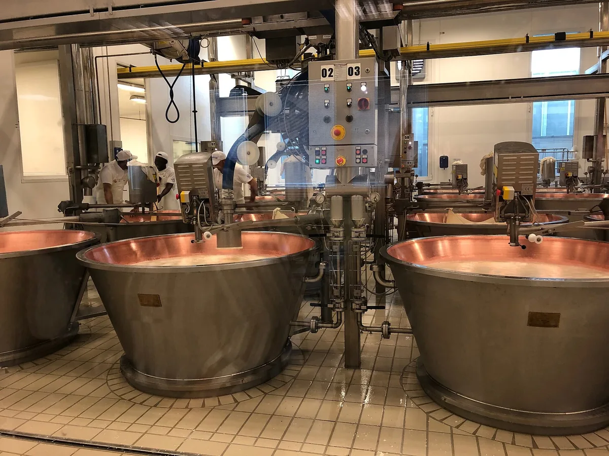 Kupferkessel und Käsemacher bei der Arbeit in einer Parmigiano-Reggiano-Käserei