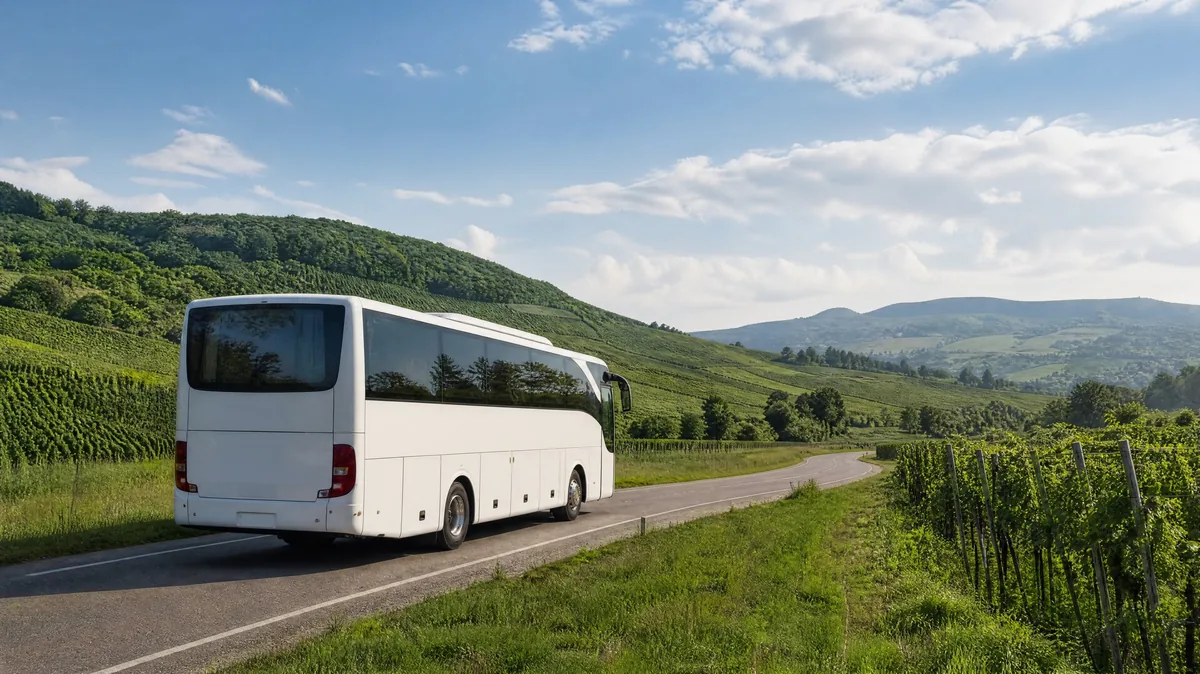 A white intercity bus on a country road between fields and low hills