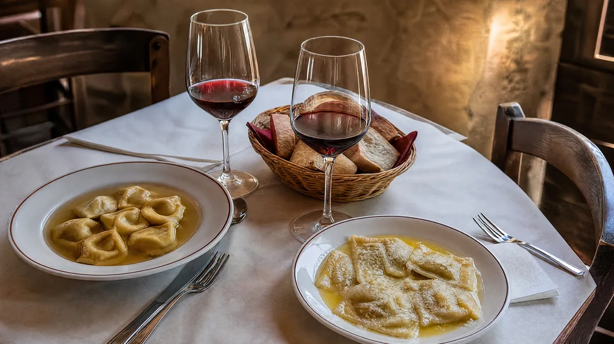 Ein Trattoria-Tisch mit anolini in Brühe, tortelli, Brot und zwei Gläsern Rotwein