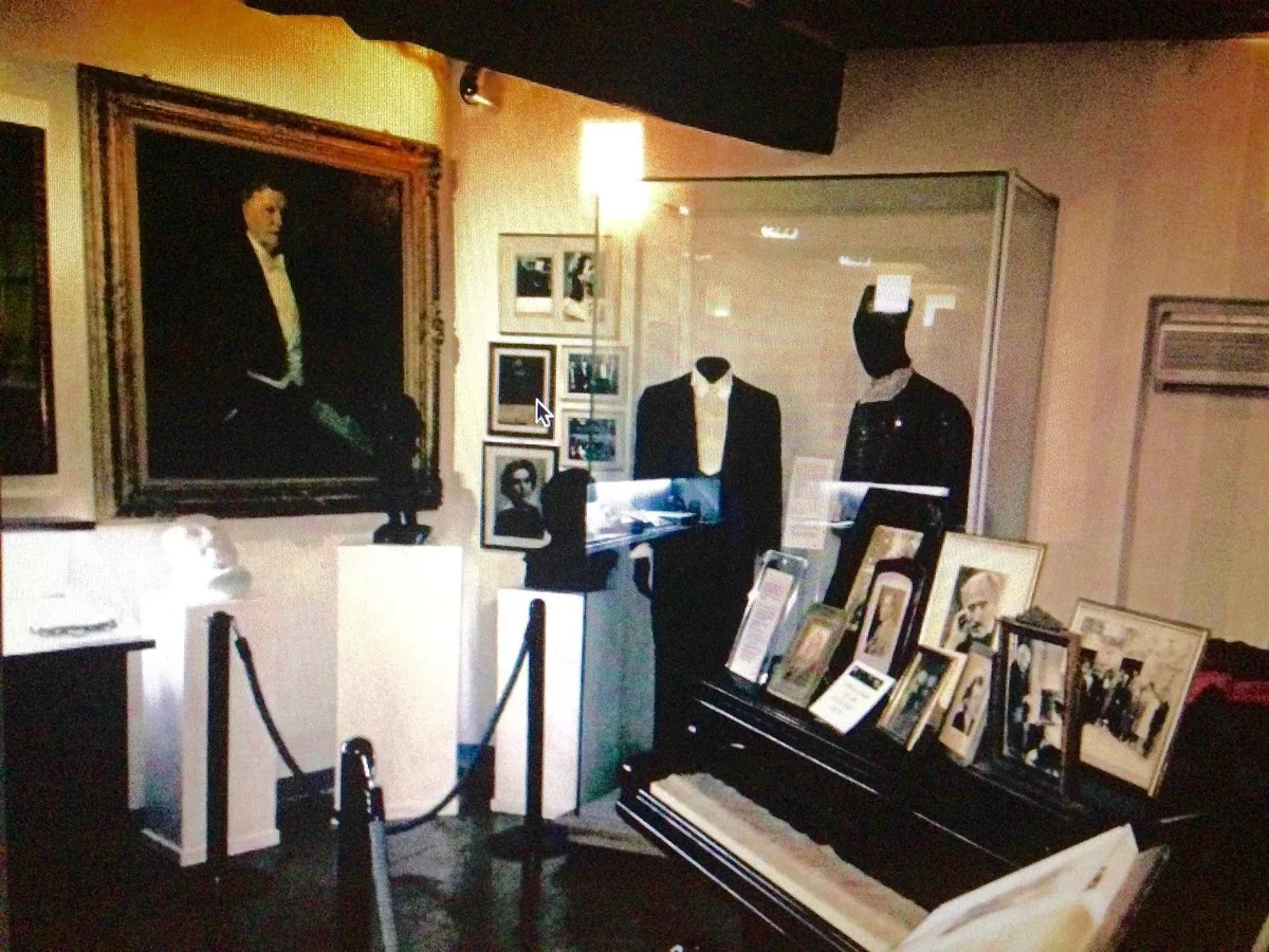 Piano room in Toscanini's birthplace with his portrait, tailcoats and framed photos